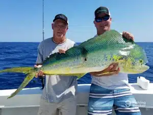 Two men proudly displaying a large fish caught during a deep-sea fishing trip.