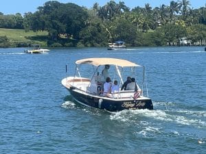 A small motorboat named "Flying Lady" with four people on board is cruising on a lake surrounded by lush greenery, invoking the serene charm of a Dolphin Boat Tour as other boats drift peacefully in the background.