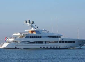 A large white luxury yacht named "Rockit," inspired by the elegance of Palm Beach Mega Yachts, sails on calm water under a clear blue sky.
