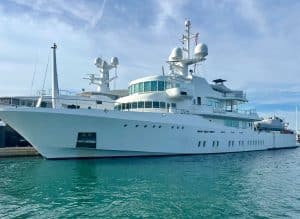 A large white luxury Palm Beach Mega Yacht docked at a marina on a sunny day, with calm turquoise water and blue sky in the background.